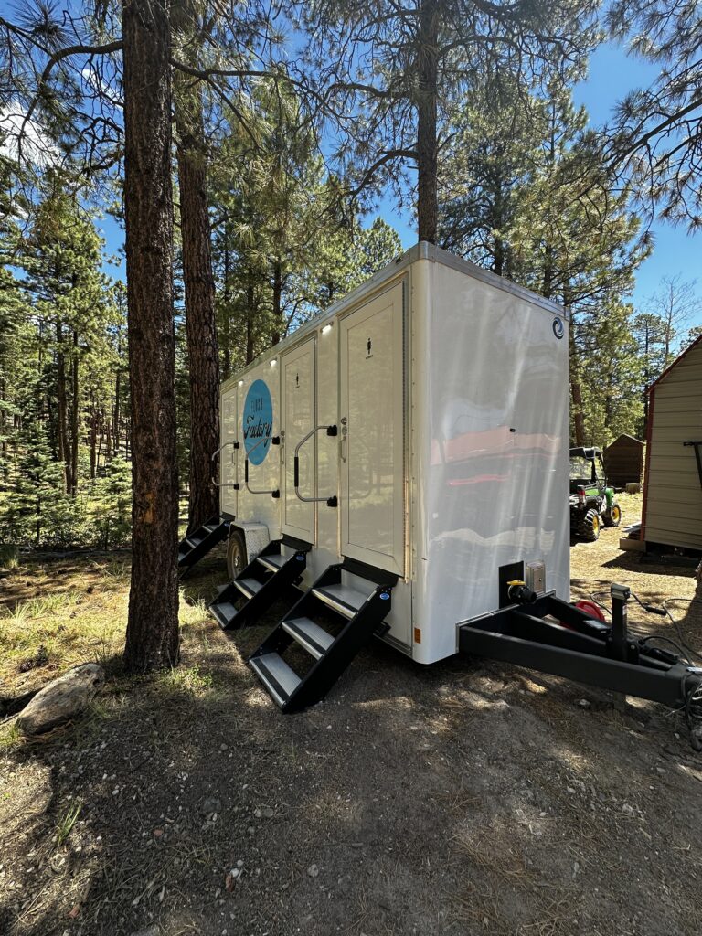 Restroom trailer set up among pine trees at a mountain venue