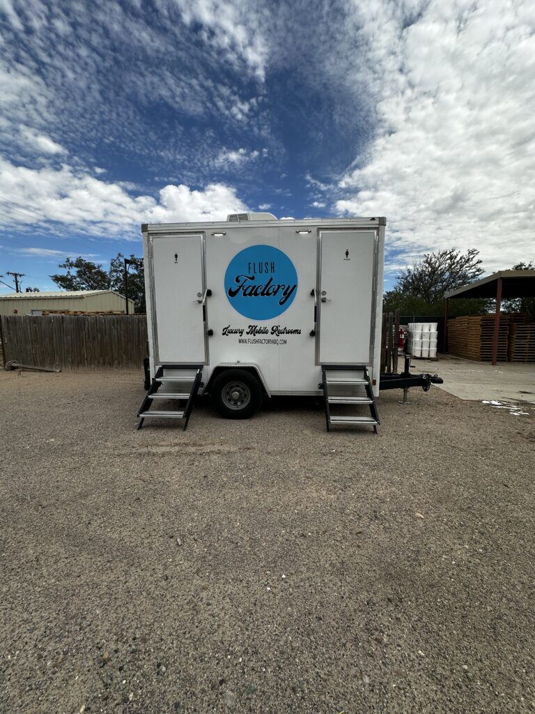 Three-stall restroom trailer with entry steps set up on a gravel lot