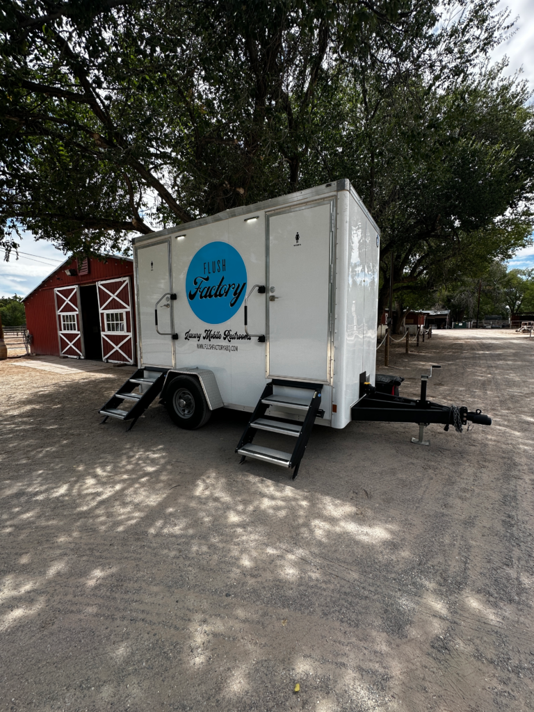 Flush Factory two-stall restroom trailer set up at a rural New Mexico property with a barn