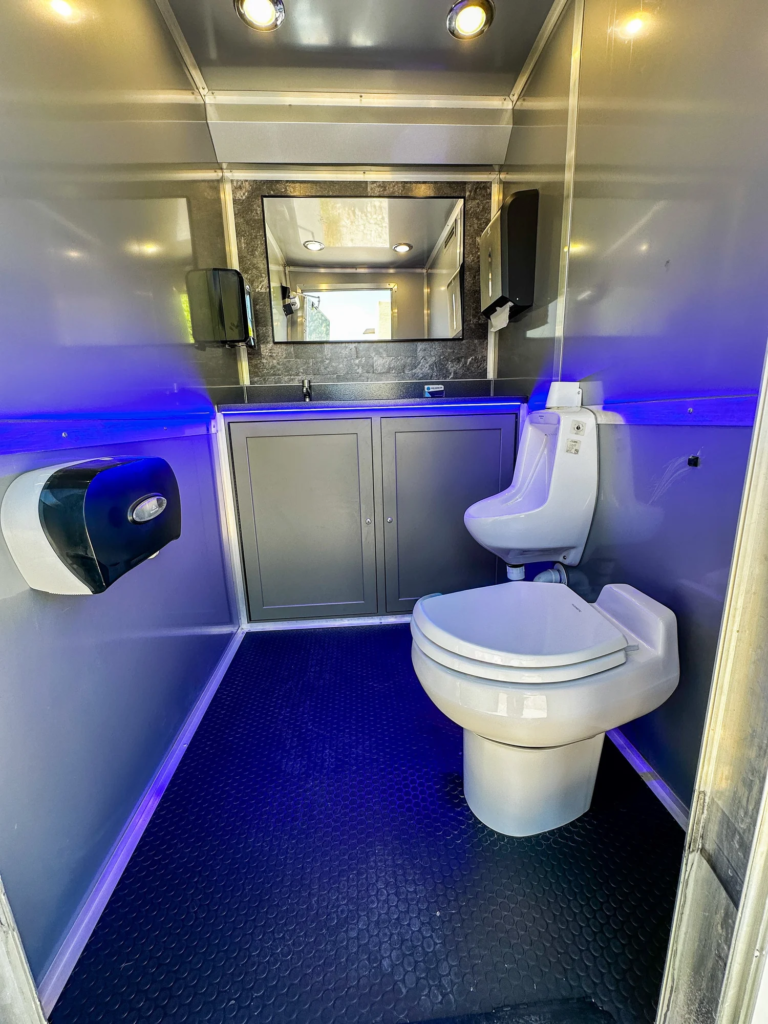 Clean restroom trailer stall with flushing toilet and blue LED lighting